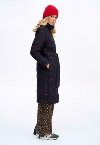 Čierny prešívaný kabát s červenými bodkami, opasok v oblasti pása a vysoký golier. V kombinácii s nohavicami v leopardom vzore a multikolorovými teniskami. Červená čiapka.