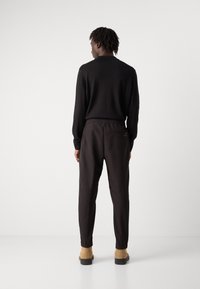 Pulover negru, ajustat, cu manșete cu model, asociat cu pantaloni jogger negri, tapered, care au un brâu elastic și buzunare laterale. Botine bej.