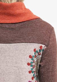 Braunes und graues Langarmoberteil mit rotem Kragen. Hat ein florales Muster und eine strukturierte Stoffqualität. Kontrastierende Farbblockierung an den Schultern.