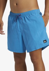 Bañadores azules hechos de material ligero, con una cinturilla elástica con cordón y un pequeño logo de la marca en el dobladillo.