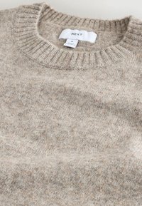 Suéter de punto beige hecho de una tela suave, con un cuello redondo acanalado y un patrón texturizado, con una etiqueta que muestra la marca y la talla.