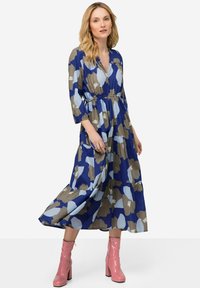 Vestido maxi en azul, marrón y azul claro con patrones abstractos; presenta un diseño en capas y una cintura elástica. Combinado con botas de tacón rosas.