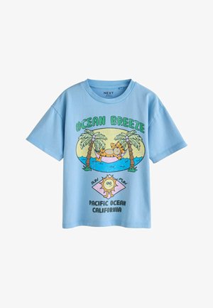 Hellblaues Kurzarmhemd mit einem Cartoon-Tiger, der in einer Hängematte zwischen Palmen entspannt, Text "Ocean Breeze" und "Pacific Ocean California."