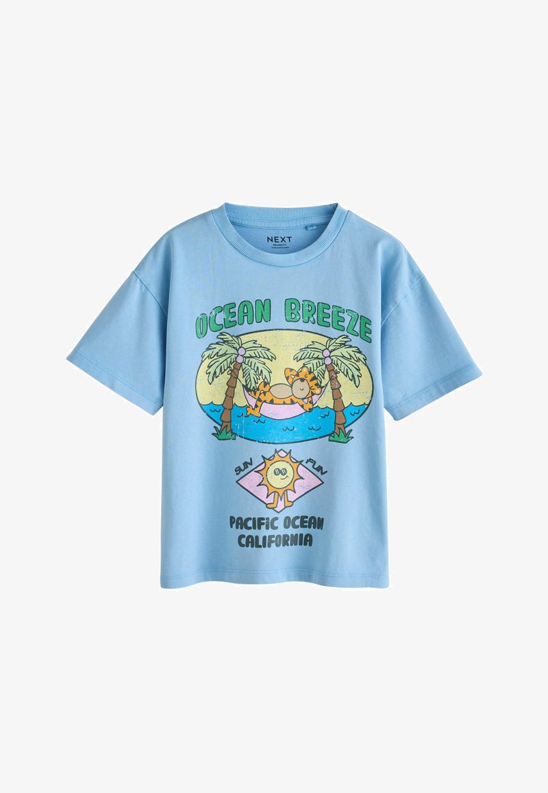 Chemise bleu clair à manches courtes avec un tigre de dessin animé se relaxant dans un hamac entre des palmiers, texte « Brise Océan » et « Océan Pacifique Californie ».