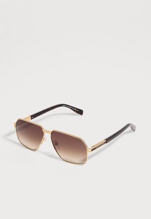 Lunettes de soleil Marc Jacobs à monture dorée avec verres carrés dégradés marron et branches noires sur un fond clair uni.
