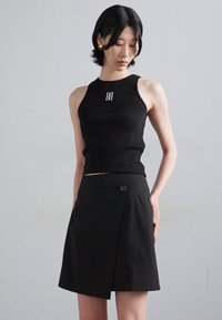 Top in cotone nero a coste con logo, abbinato a una gonna avvolgente nera con dettaglio dei bottoni. Entrambi i capi hanno un design aderente.
