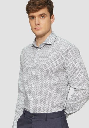 Witte shirt met geometrisch zwart patroon, met knoopsluiting, lange mouwen en een getailleerde pasvorm, gecombineerd met donkere broek.
