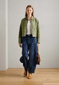 Kvaliteediga oliivroheline jakk, valge topp, tumedate mustritega laiade pükste paari, beežid pahkluu saapad ja pruun õlakott. Sile tekstuur.