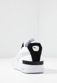 Białe sneakersy z gładką skórzaną cholewką, czarnym zamszowym kontratowym, złotym akcentem logo i teksturowaną gumową podeszwą.