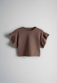 Hnedý krátky krátkym rukávom crop top s volánikmi na rukávoch, položený na svetlosivom povrchu.