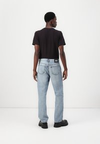 Zwarte T-shirt met korte mouwen, lichtblauwe spijkerbroek met rechte pasvorm, en zwarte chunky schoenen. De spijkerbroek heeft contrasterende stiksels.