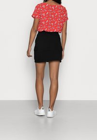 Červený květinový top s krátkým rukávem, černá přiléhavá sukně s bočními kapsami, bílé boty. Důraz na barevný kontrast a minimalistické designové prvky.