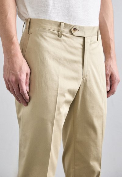 Beige zúžené kalhoty vyrobené z lehkého materiálu, s předním zipem, zapínáním na knoflík a jemnými puky po stranách nohavic.