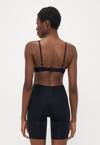 Svart bh med tynne justerbare stropper og krokfeste, kombinert med svarte høye shorts, begge laget av glatt, elastisk stoff.