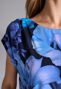 Kwiatowa bluzka z dużymi niebieskimi kwiatami na czarnym tle. Materiał jest lekki o gładkiej fakturze i szerokich rękawach.