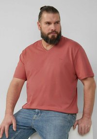 Lockere V-Ausschnitt-T-Shirts in staubigem Rosa, aus weicher Baumwolle. Kurze Ärmel, dezentes Logo auf der Brust, kombiniert mit blauen Jeans.