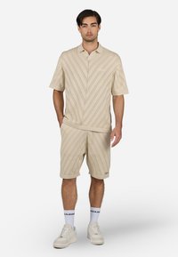 Un polo beige clair à manches courtes et un short assorti présentent un design à rayures diagonales texturées. Tissu doux avec une coupe décontractée et des accents subtils.