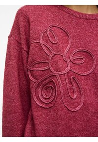 Pull bordeaux en maille avec un motif floral texturé en applique. Il présente un col rond et une coupe ample, fabriqué dans un matériau doux et chaud.