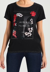 Top negro de manga corta con un diseño gráfico floral que presenta flores rojas y blancas, texto, y un cuello y dobladillo texturizados.