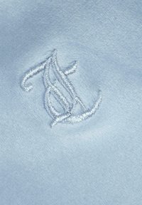 Ljusblått tyg med mjuk textur som har ett framträdande broderat monogram i vit tråd, detaljerat och intrikat utformat.