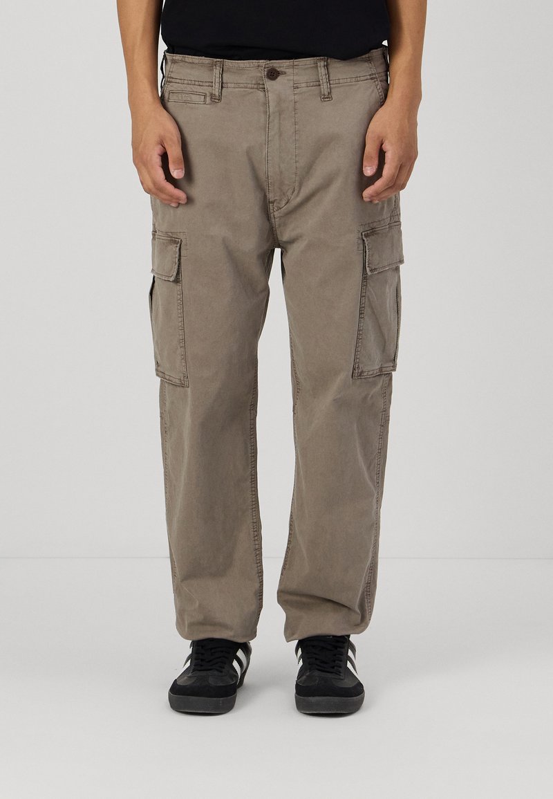 Beige cargo bukser laget av bomullsblend, med flere sidelommer og rett ben-design. Kombinert med svarte joggesko.