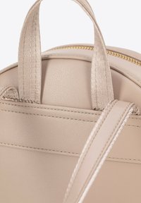 Zaino beige in pelle testurizzata, con manici superiori e una tracolla, rifinito con cuciture a contrasto e una cerniera dorata.