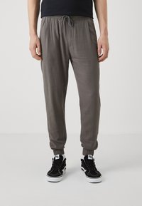 Pantalones de chándal grises con cintura elástica y cordón, con tobillos ajustados y un material ligero y texturizado. Combinados con zapatillas negras.