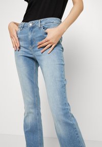 Jeans in denim azzurro chiaro con vestibilità standard, cinque tasche e chiusura a zip con bottone. Leggero sbiadimento del tessuto.