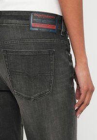 Μαύρα τζιν από denim με εμφανή πίσω τσέπη, αντίθετη ραφή και δερμάτινο μοτίβο με κείμενο σε κόκκινο και μπλε.