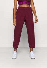 Burgunderfarvede cropped sweatpants med elastisk talje og side-striber. Blødt stof med synlige stikninger; parret med hvide sneakers.