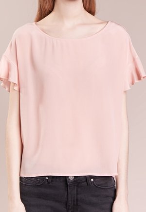 Blouse rose clair à manches courtes avec manches à volants, encolure ronde, portée sortie sur un jean noir.