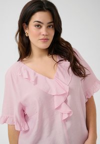 Blusa rosa chiaro con scollo a V, dettagli arricciati sul davanti e sulle maniche, realizzata in un tessuto testurizzato.