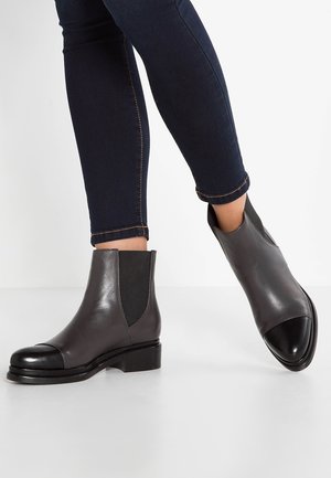 Bottes cheville en cuir gris avec embout noir, panneaux latéraux élastiques, talon bas et texture lisse, assorties à un jean ajusté bleu foncé.