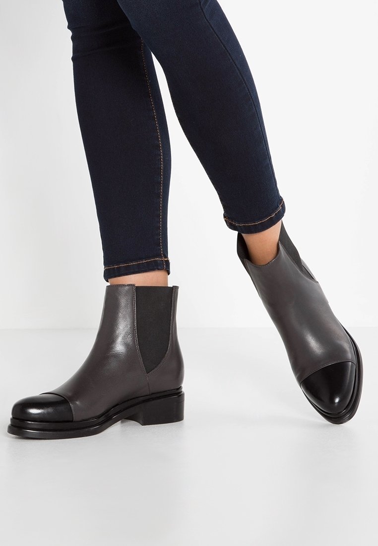 Bottes cheville en cuir gris avec embout noir, panneaux latéraux élastiques, talon bas et texture lisse, assorties à un jean ajusté bleu foncé.