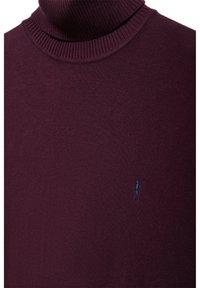 Pull à col roulé côtelé bordeaux avec un petit logo brodé bleu foncé représentant une personne portant un club de golf sur la poitrine.