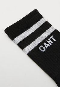 Calzino nero con due righe orizzontali bianche sulla parte superiore e logo "GANT" in carattere bianco. Realizzato in un materiale a maglia elasticizzato.