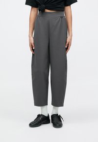 Szürke, magas derekú nadrág laza szabással és rugalmas derékpánttal. Sima anyag, oldalzsebekkel és finom varrási részletekkel. Fekete tornacipővel viselve.