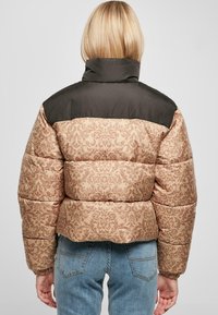 Pufferjakke med et beige ornamentalt mønster og mørkegr�ønne skuldre. Designet er cropped og fylt for isolasjon.