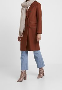 Brun uldblandet frakke med to forlommer, parret med lyseblå denim flared jeans og brune blokhælede ankelstøvler med slangeskindsprint.