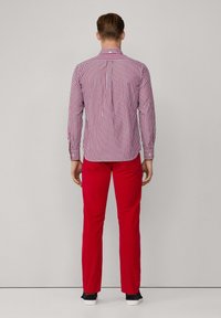 Pantalones rojos combinados con una camiseta de rayas multicolores que presenta líneas horizontales y verticales, puños abotonados y detalle de pliegue en la espalda.