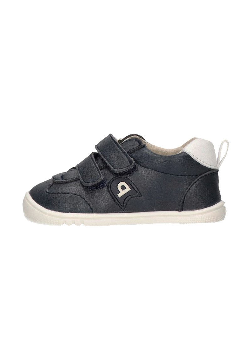 Zapatilla negra de cuero con dos tiras de velcro, acentos en blanco, puntera redonda y suela de goma texturizada. Pequeño detalle del logo en el lateral.