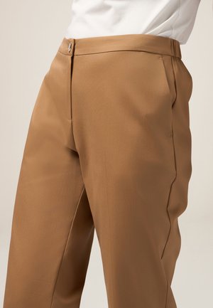 Pantaloni beige su misura con una texture liscia, dotati di tasche laterali, una chiusura frontale e pieghe nette sul davanti.