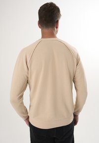 Beige Sweatshirt mit langen Ärmeln, gerippten Bündchen und Rundhalsausschnitt. Verfügt über eine rohes Kantennaht entlang des Rückens und eine weiche Stofftextur.
