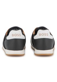 Black athletic shoes with a perforated design, featuring a white heel cap with "BOSS" in rose gold. Rubber sole with a tan accent.