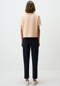 Perzikkleurig cropped top met korte mouwen, gecombineerd met marineblauwe op maat gemaakte broek en witte sneakers, gezien van achteren.