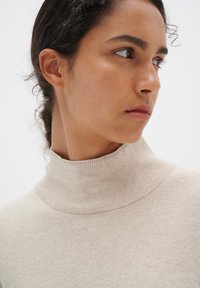 Beige turtleneck sweater with a soft texture, fitted design, and ribbed neck and hem detailing, against a plain white background.