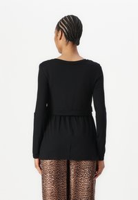Svart langermet topp med en avslappet passform, med belte i midjen, kombinert med brune bukser med leopardmønster og vide bein.
