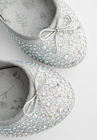 Bailarinas plateadas con un upper texturizado cubierto de brillantes de colores, con un pequeño lazo en la puntera.