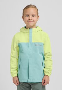 Chaqueta ligera bicolor en amarillo brillante y verde azulado, con capucha, cremallera frontal y bolsillos laterales. Presenta puños elásticos y un detalle de logo.