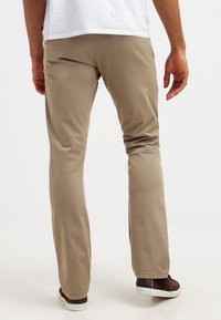 Béžové chino kalhoty s úzkým střihem, vyrobené z hladké bavlněné látky. Mají boční kapsy a čistý lem. Nošeny s bílými teniskami.